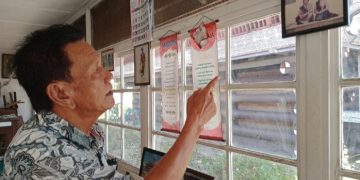 Drs Djomen Purba sedang menunjukkan foto penabalan Edwin Bingei Purba Siboro dengan istrinya boru Damanik. (foto : HTP)