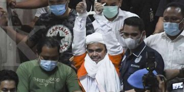 Rizieq Shihab berjalan menuju mobil tahanan usai diperiksa di Mapolda Metro Jaya, Jakarta, Minggu (13/12/2020) dini hari.
